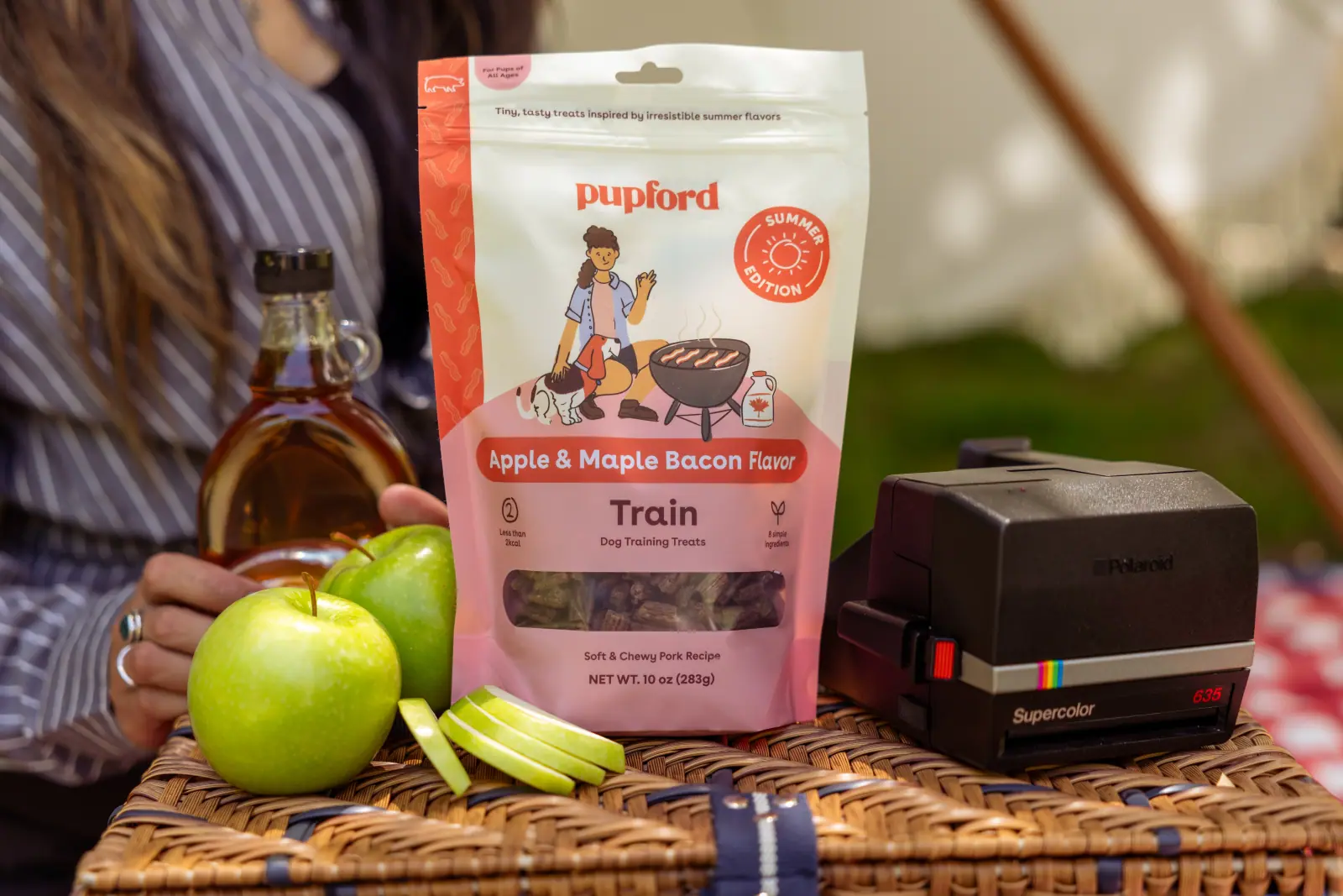 A Pupford Train bag standing with green apples and a wooden crate on a picnic table