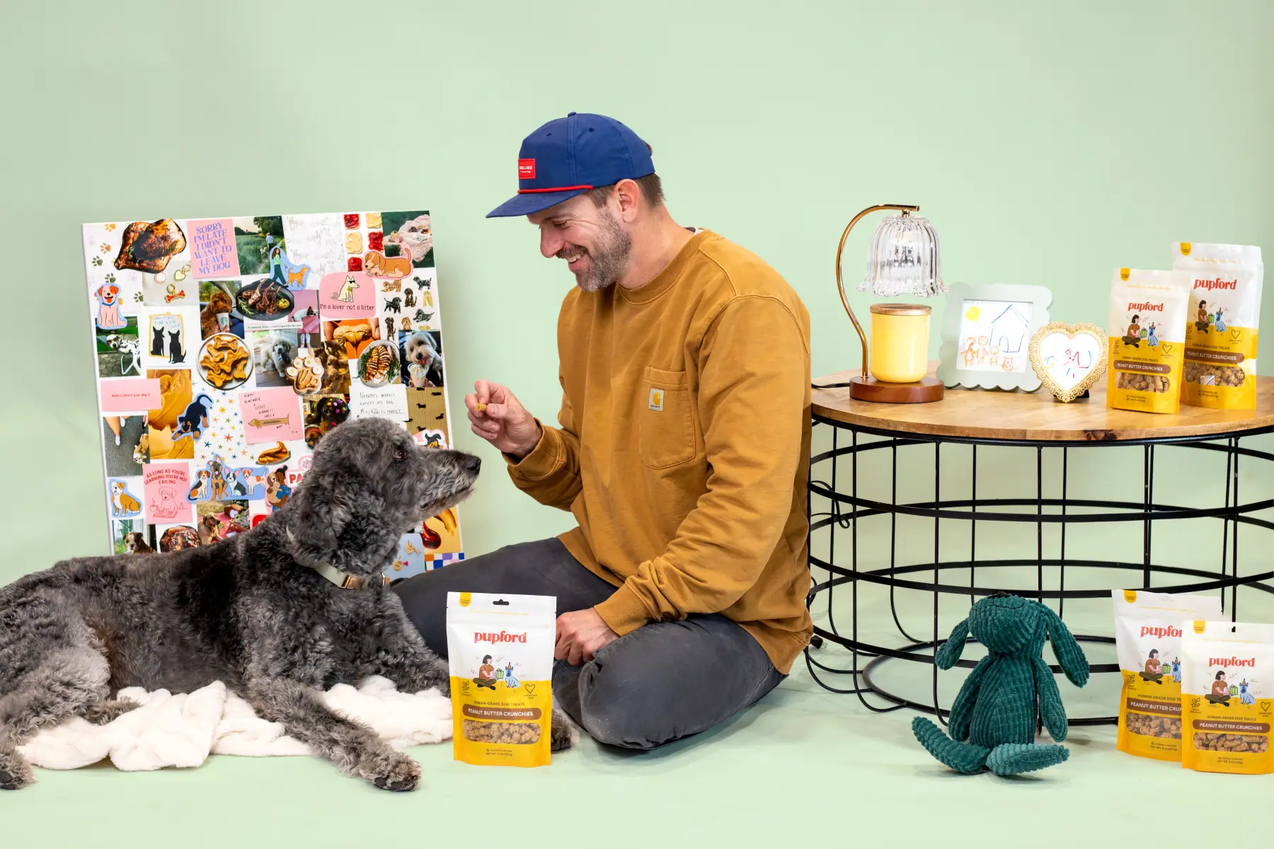 Man sitting on a green studio set with two dogs and a Pupford product display
