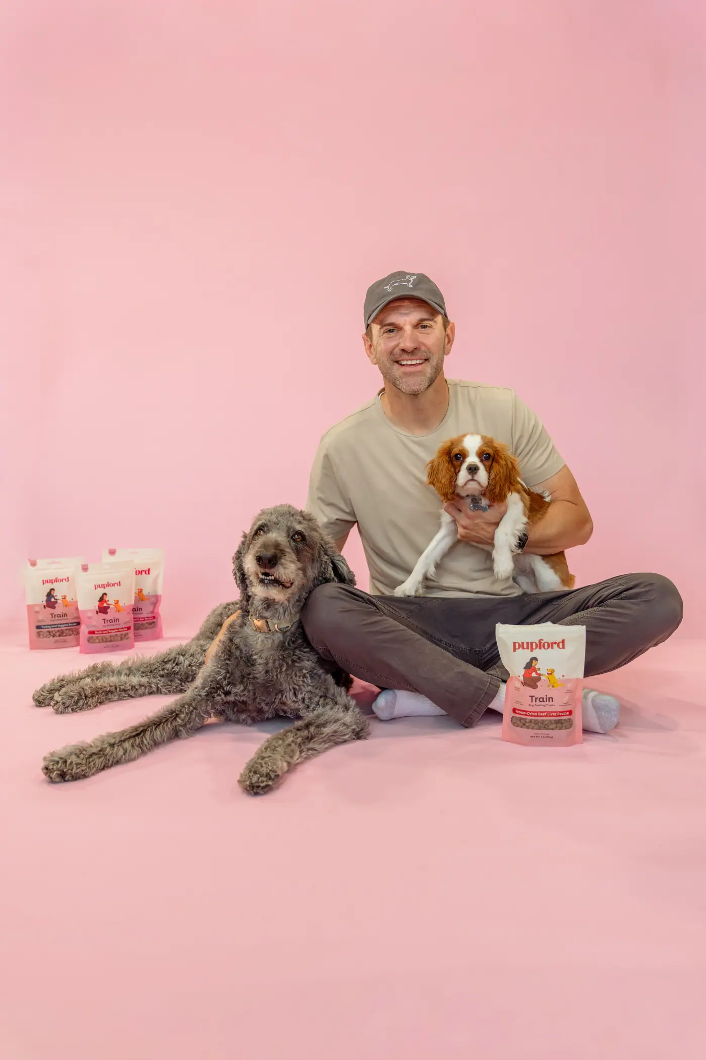 Man sitting with two dogs and Pupford bags on a pink studio background