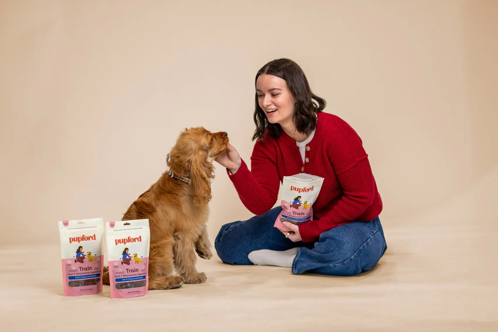 Woman kneeling with a golden dog and Pupford bags on a warm studio background